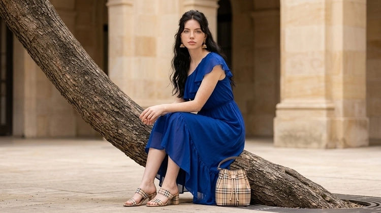 A beautiful woman in a royal blue dress seated on a tree trunk in an urban courtyard